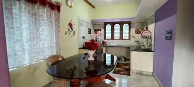 a dining room with a glass table and a kitchen at Greeneysthomestay in Kushālnagar