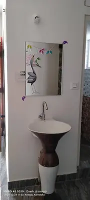 a bathroom sink with a mirror and a bird picture at Greeneysthomestay in Kushālnagar