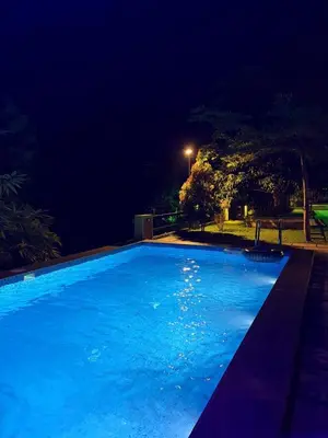 a large blue swimming pool at night at Maple grove villa resort in Panamaram