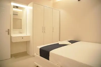 a white bedroom with a bed and a cabinet at Gentur Enclave in Mananthavady
