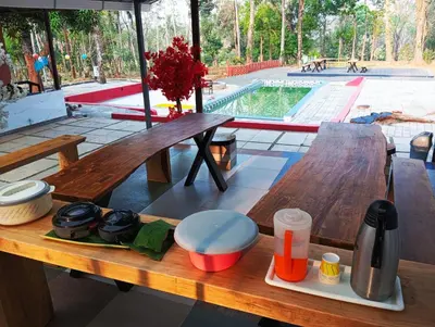 a wooden picnic table with a pool in the background at The Multi Gen Retreat at gaya3farms in Parli