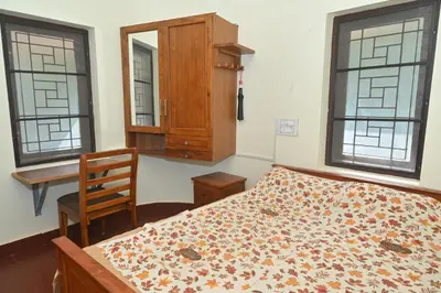 a bedroom with a bed and a dresser and two windows at Nisarga Greens in Chittūr