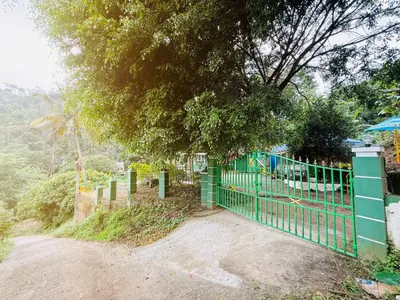 a green fence next to a dirt road with a tree at Greenwoods Mist Villa in Munnar
