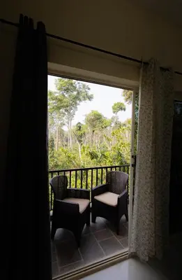 a room with a balcony with chairs and a window at Bougain Villa in Madikeri