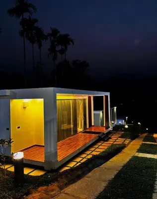a small house with a wooden deck at night at West wind Resort in Meppādi