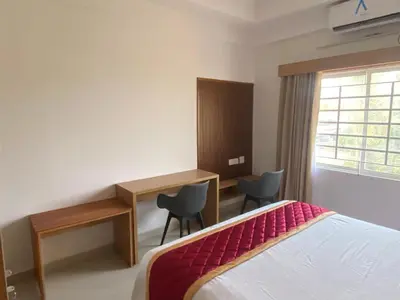 a bedroom with a bed and a desk and a window at Nova Alhind Airport Hotel in Nedumbassery
