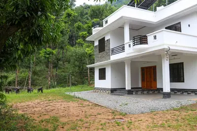 a white house with a dog in front of it at Surya Homestay in Marayoor