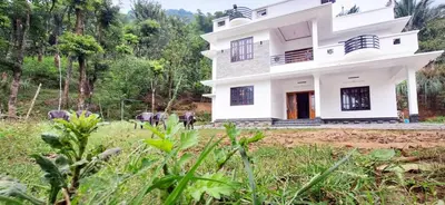 a white house in the middle of a field at Surya Homestay in Marayoor