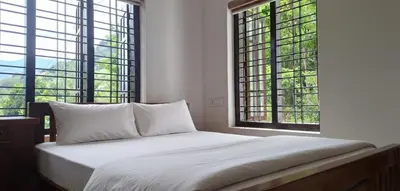 a white bed in a room with two windows at Surya Homestay in Marayoor