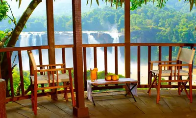 a porch with two chairs and a table with a view of a waterfall at Rainforest Resort in Athirappilly