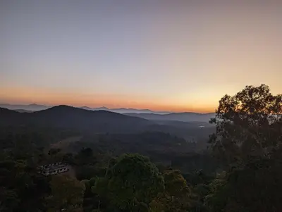 a sunset over the mountains with a house in the foreground at Oxyrich Business Class Hotel in Madikeri