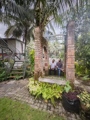 two men sitting on a brick wall under a palm tree at Akshaya Homestay in Trichūr