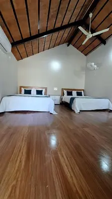 two beds in a large room with wooden floors at Bombe Resort Channapatna in Channapatna