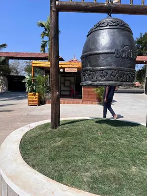 a person walking past a large bell hanging from a pole at Bombe Resort Channapatna in Channapatna