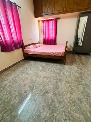 a bedroom with a bed with pink curtains and a concrete floor at RoBen Villa in Pollāchi