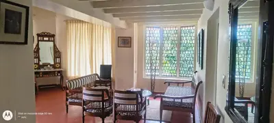 a living room with chairs and a table and windows at Amblyn Home stay coorg in Madikeri