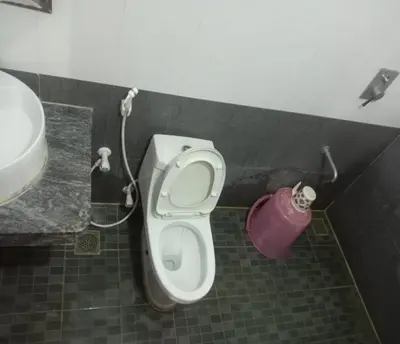 a bathroom with a toilet and a pink bucket at Blue Stones Service Apartment in Coimbatore