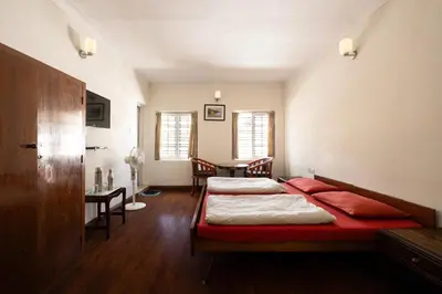 two beds in a room with a table and chairs at Colonels inn in Ooty