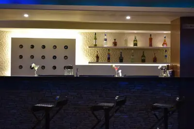 a bar with four stools in a room with bottles at Kiscol Grands Hotel in Coimbatore