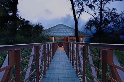 a wooden bridge leading to a pavilion with a building at The IBNII - Eco Luxury Resort in Madikeri