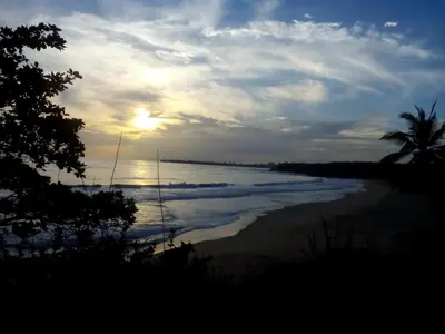 a sunset on a beach with a boat in the water at Ivory Coaste in Kannur