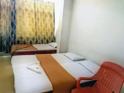 two beds in a room with a red chair at Hotel Ashwini Lodge in Mysore