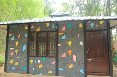 a small house with a mosaic wall and a door at Greenwoods Nature Camp in Mudumalai National Park