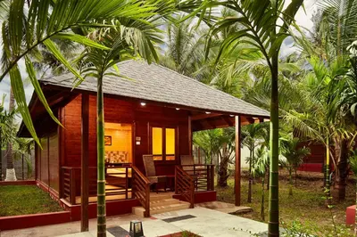 a wooden cabin with a porch and palm trees at Sterling Anaikatti in Varagampadi