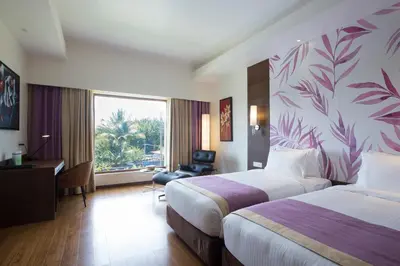 a hotel room with two beds and a desk and a window at Purple Palms Resort & Spa in Kushālnagar