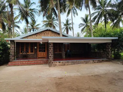 a brick building with palm trees in the background at Green Acres Farm Guest House in Masinagudi