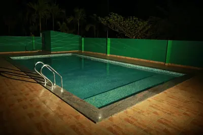 a swimming pool at night with a green wall at Palm Era Resorts in Kushālnagar