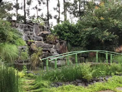 a green bridge over a pond with a waterfall at Palm Era Resorts in Kushālnagar