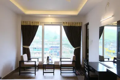 a living room with a table and chairs and large windows at Jays Inn in Munnar