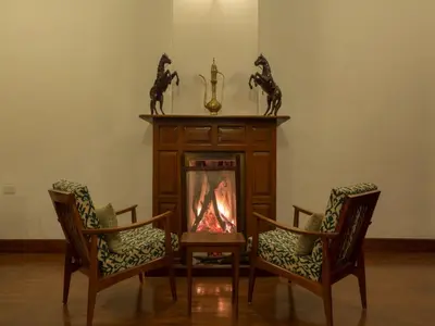 a living room with two chairs and a fireplace at SaffronStays Milton Abbott Estate - 2BR colonial-era bungalow with garden, golf course views & bonfire nights near Ooty Golf Club in Ooty