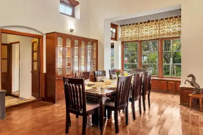 a dining room with a table and chairs and windows at SaffronStays Milton Abbott Estate - 2BR colonial-era bungalow with garden, golf course views & bonfire nights near Ooty Golf Club in Ooty