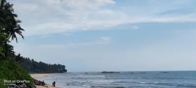 a beach with people standing on the sand and the ocean at White Shell Beach House in Kannur