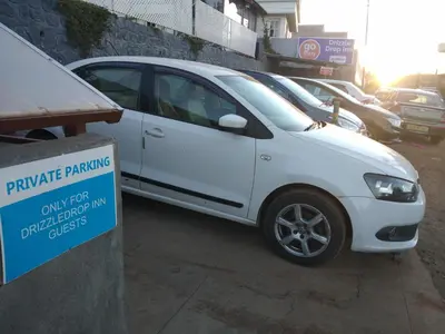 a white car parked in a parking lot with a parking sign at Drizzle Drop Inn in Ooty