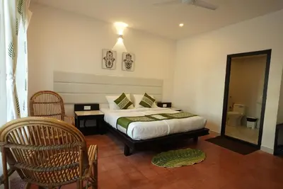 a bedroom with a bed and two chairs and a mirror at Veda5 Ayurveda Living Village in Trichūr