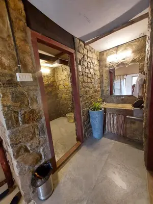 a room with a stone wall and a bathroom at Deshadan Eco Valley Resort - An Eco friendly Mud House in Kanthalloor