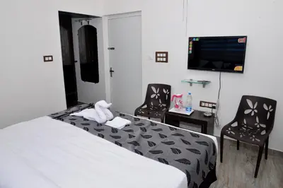 a hotel room with a bed and two chairs and a tv at Suroor Tourist Home in Virajpet