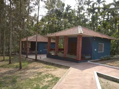 a small blue house in the middle of trees at The Shades Holiday Homes in Kushālnagar