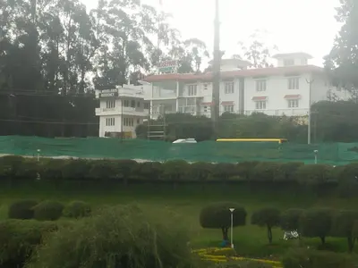 a green field with a white building in the background at Rosepark Residency in Ooty