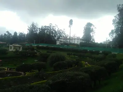 a garden with many bushes and trees and a building at Rosepark Residency in Ooty