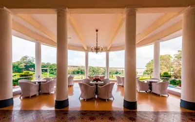 a large room with columns and a dining room with tables and chairs at Royal Orchid Brindavan Garden Palace & Spa Mysore in Belagula