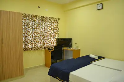 a bedroom with a bed and a desk and a window at Golden Nest in Mysore