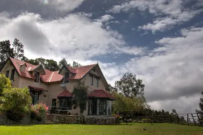 a house with a red roof on a green field at Stumpfields in Ooty