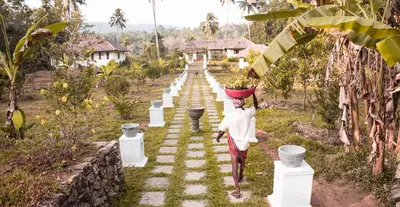 a woman carrying a basket on her head walking down a path at Windermere River House in Neriyamangalam