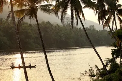 people in a boat on a river with palm trees at Windermere River House in Neriyamangalam