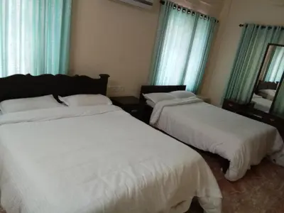 two beds in a room with blue curtains and windows at Anandkrishna Residency in Guruvāyūr