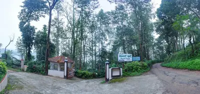 a dirt road with a sign next to a forest at Royal Woods Coorg in Madikeri